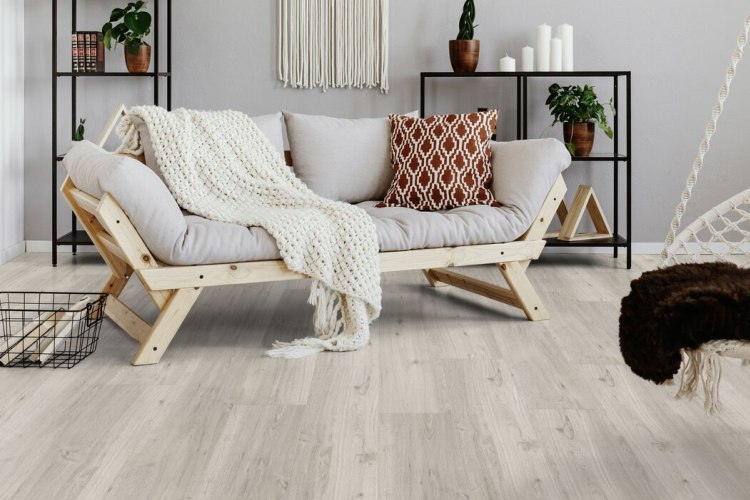 Salon lumineux avec canapé bohème et étagères en bois posés sur un sol en lames PVC imitation chêne clair