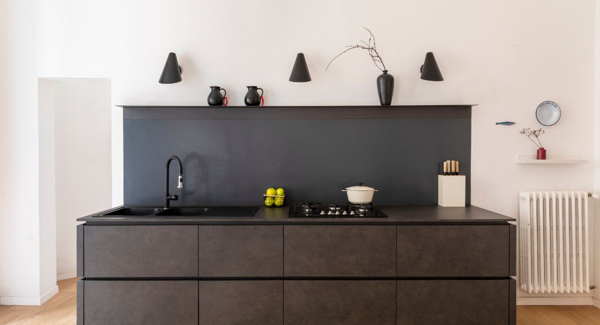 Voici une cuisine moderne et élégante avec un îlot central sombre, un évier noir, une plaque de cuisson et des luminaires noirs sur un mur blanc.