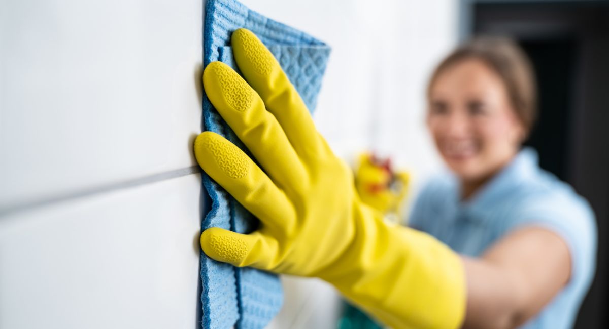 personne qui nettoie des joints de carrelage avec une éponge et des gants jaunes pour se protéger les mains