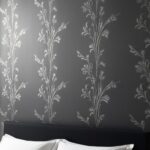 Papier peint tête de lit pour chambre adulte, noir mat avec un motif floral stylisé argenté. Imaginez une chambre avec un lit en bois sombre, une parure de lit blanche et des tables de chevet en métal noir. Le papier peint noir met en valeur le mobilier et crée une ambiance élégante et raffinée.