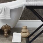 Une salle de bain avec une baignoire blanche sur des pieds dorés. Des serviettes blanches sont empilées sur une table noire et il y a des paniers tressés sur le sol.