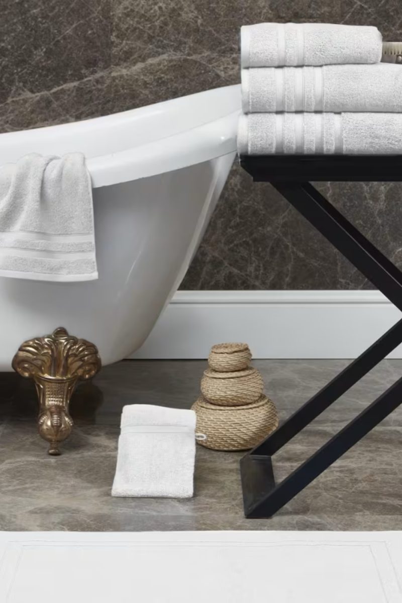 Une salle de bain avec une baignoire blanche sur des pieds dorés. Des serviettes blanches sont empilées sur une table noire et il y a des paniers tressés sur le sol.