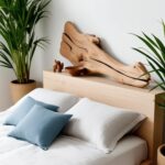 Le lit en bois clair, habillé de lin blanc et de coussins bleus, est sublimé par une tête de lit originale en bois flotté. Des plantes vertes et des objets de décoration artisanaux renforcent l'ambiance naturelle de la pièce.
