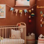 une chambre d'enfant avec une décoration terracotta et colorée. Le mur est peint dans une teinte rouille chaude et sert de toile de fond à un mélange d'éléments décoratifs.