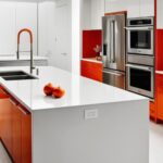Une cuisine moderne blanche et orange vif. Une île blanche et orange domine la pièce, avec un évier et deux oranges dessus.