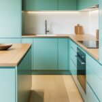 Une cuisine moderne couleur vert d'eau présente des armoires épurées, un comptoir en bois clair et un évier blanc, le tout illuminé par un éclairage sous les armoires.