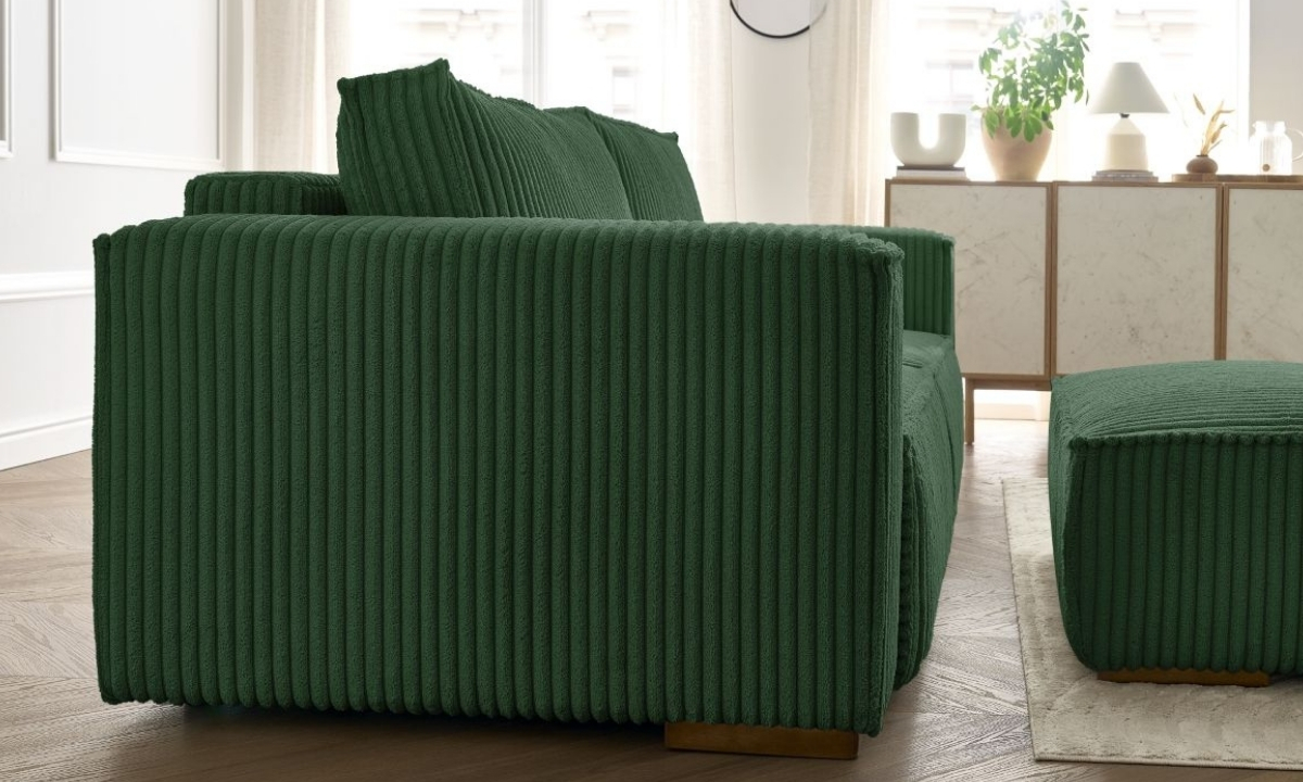 Un canapé en velours côtelé vert forêt est présenté dans un intérieur lumineux. Un pouf assorti repose sur un tapis clair à proximité d'une commode.
