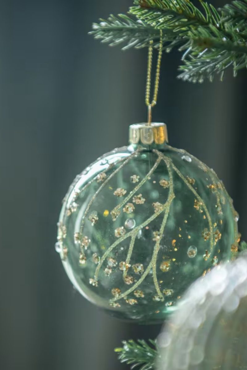 Une boule de Noël turquoise ornée de paillettes dorées est suspendue à un sapin de Noël, créant une ambiance festive et chaleureuse.
