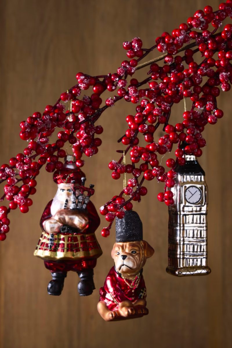 Des décorations de Noël, dont un Père Noël écossais, un bouledogue en uniforme et Big Ben, pendent à des branches de houx rouges devant un fond marron.