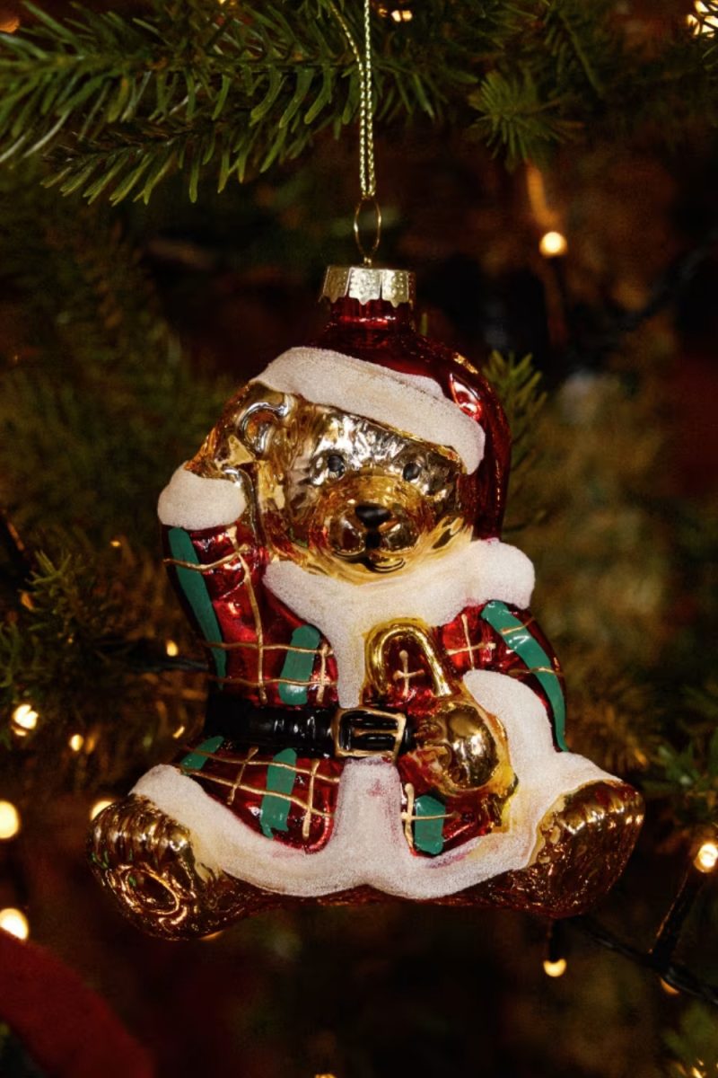 Un ornement d'ours en peluche de Noël, rouge et or, suspendu à un arbre de Noël. La figurine est décorée de détails de fourrure blanche et tient un cornet.