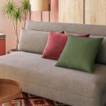 Un canapé gris neutre est agrémenté de coussins colorés dans un salon, avec une table basse à deux niveaux et un tapis à motifs ethniques.