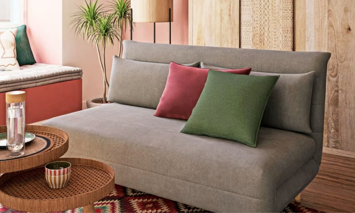 Un canapé gris neutre est agrémenté de coussins colorés dans un salon, avec une table basse à deux niveaux et un tapis à motifs ethniques.
